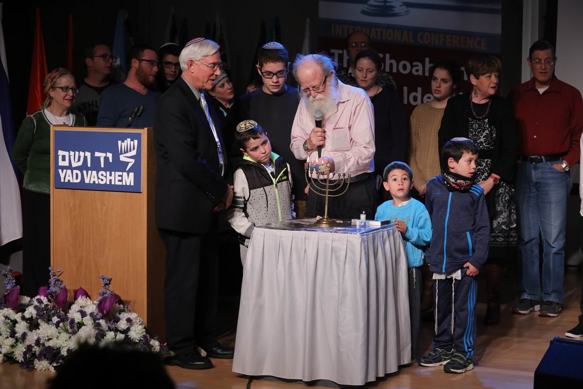 Yehuda Mansbach lights the menorah that belonged to his grandparents, Rabbi Akiva and Rachel Posner of Kiel, Germany, surrounded by his children and grandchildren